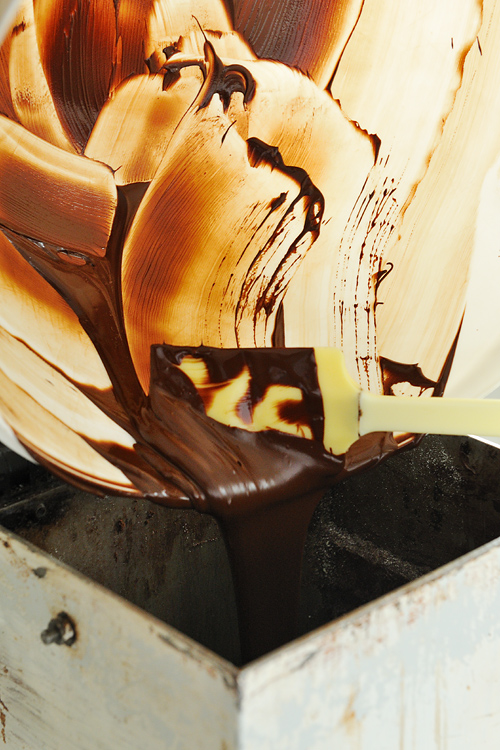 Warme, flüssige Schokolade wird aus einer Plastikschüssel zurück in die Rührtrommel gegossen